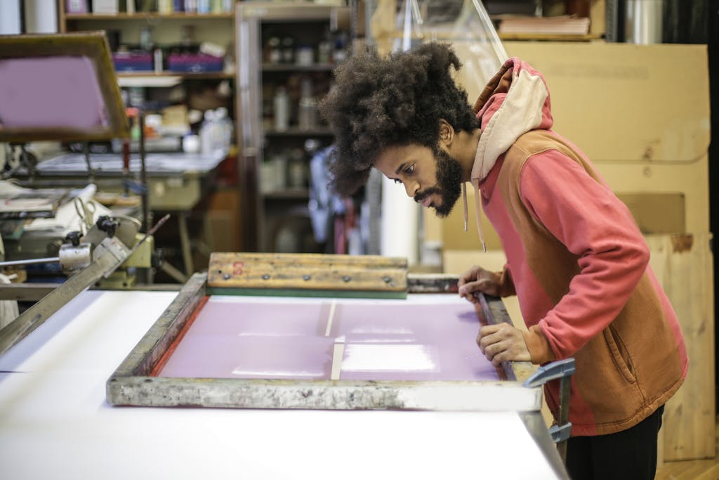 Creative young ethnic craftsman working with screen printing in workshop